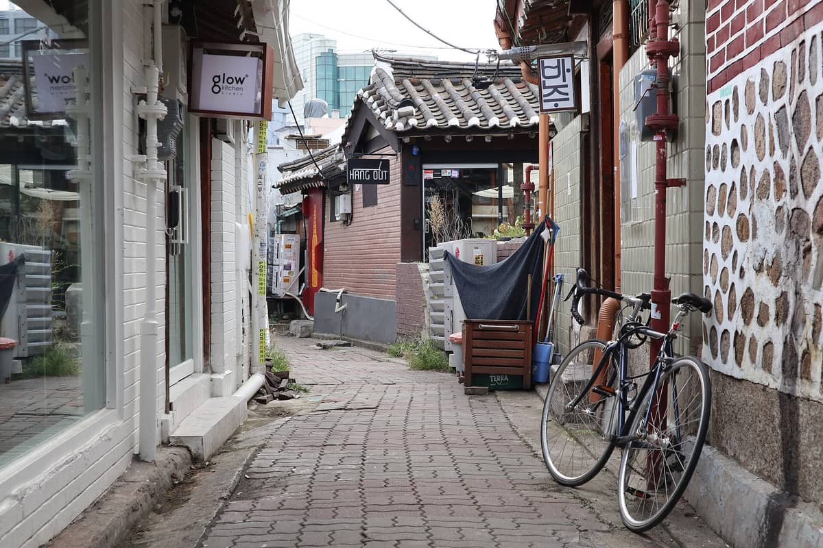 Beco estreito na Vila Hanok de Ikseon-dong com casas hanok de telhados de telha tradicional, cafés e uma bicicleta encostada na parede.