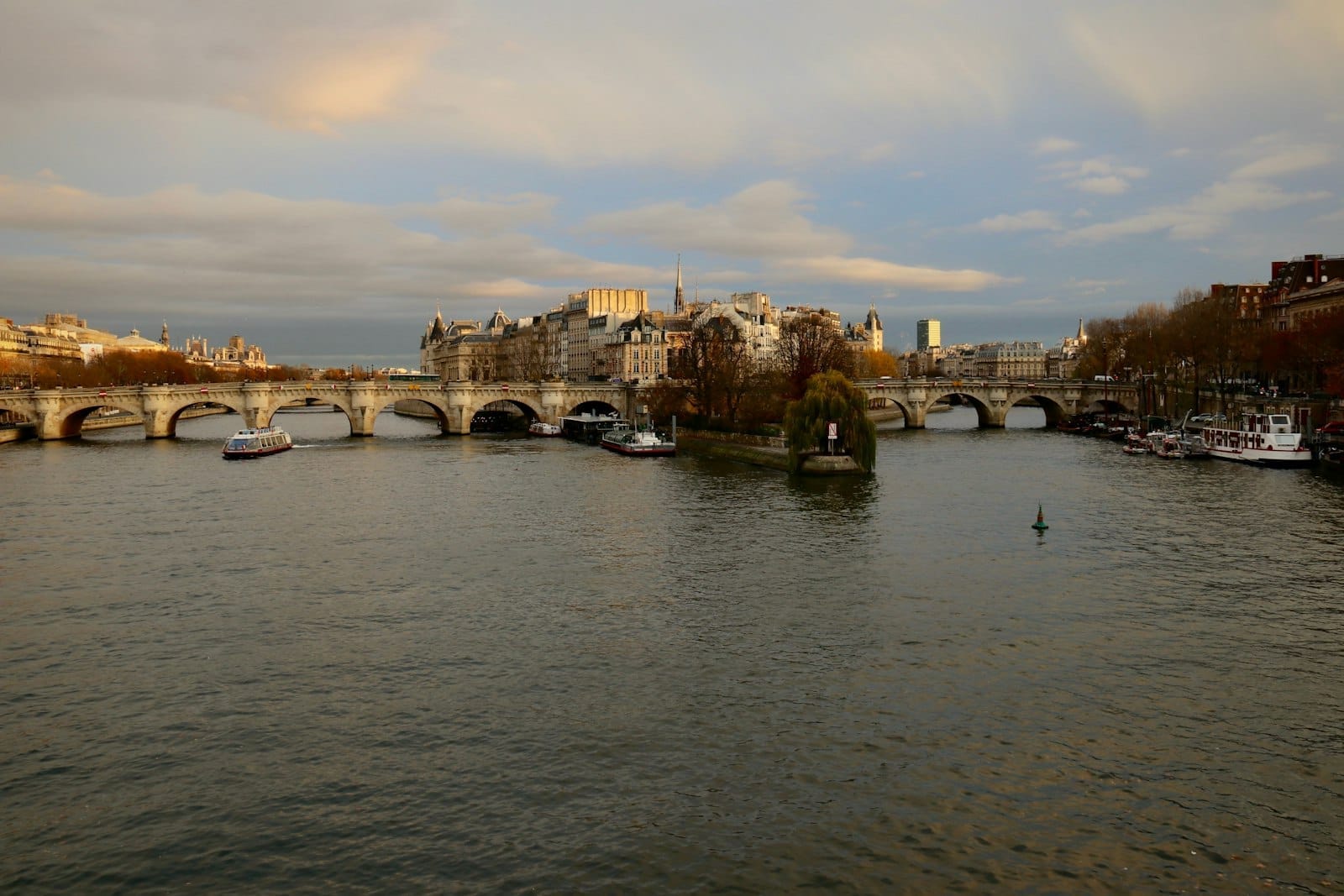 Vista dalla Senna sull'Île de la Cité con i suoi edifici storici e i ponti ad arco al tramonto, il panorama di Parigi immerso in una luce dorata.