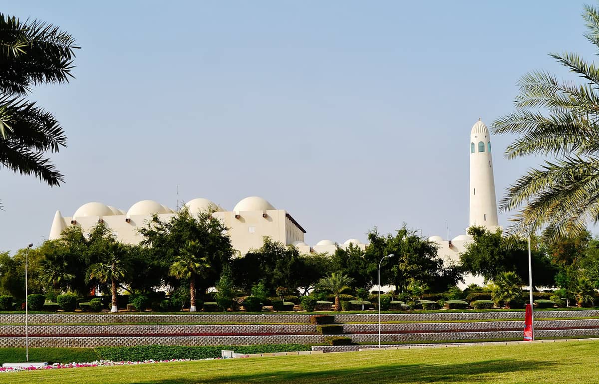 Blick auf die Imam-Muhammad-ibn-Abd-al-Wahhab-Moschee in Doha, Katar, mit ihren weißen Kuppeln und dem hohen Minarett über üppig grünen Gärten.