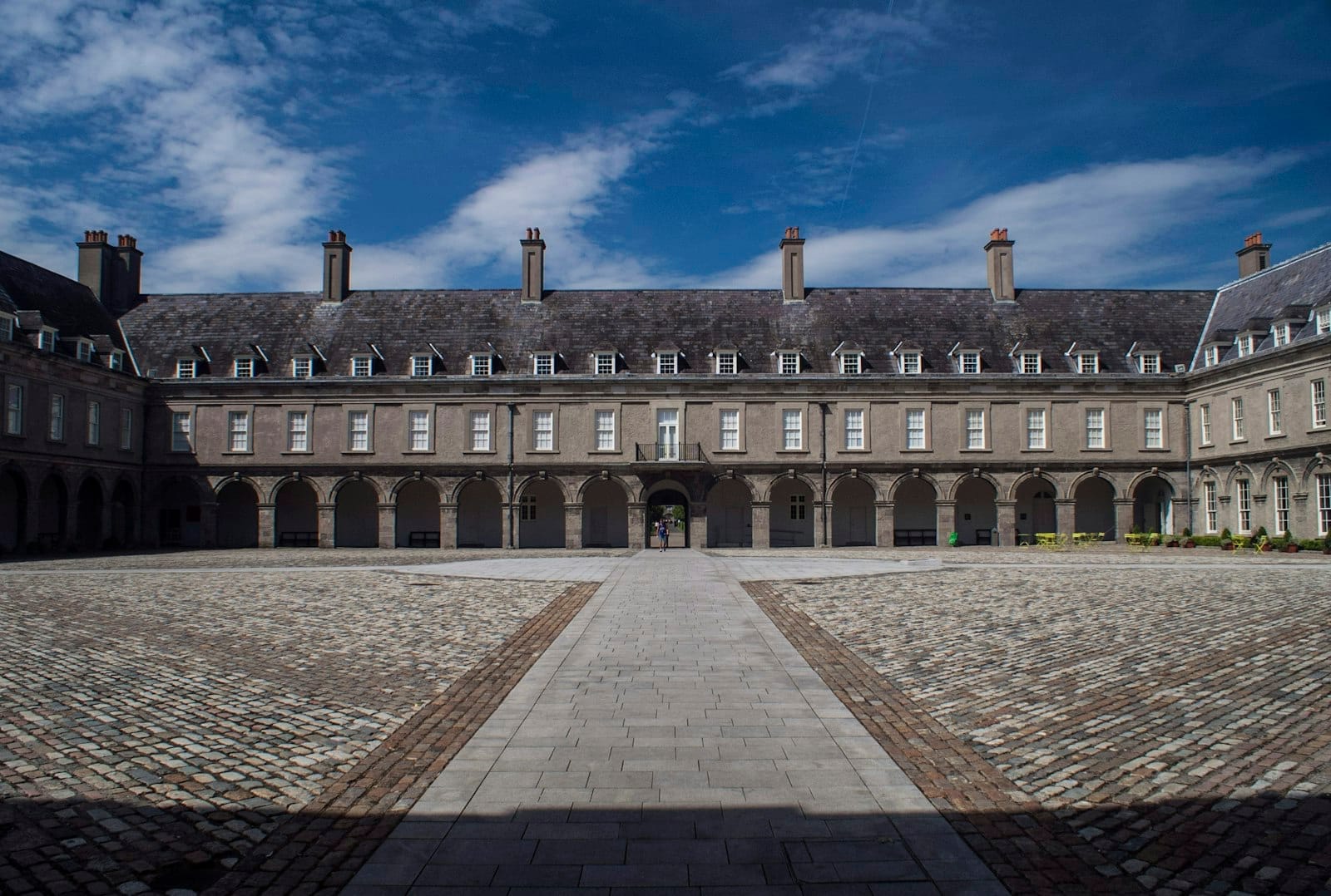 Vista grandangolare del cortile lastricato del Royal Hospital Kilmainham con la sua facciata storica sotto un cielo azzurro brillante, che mette in risalto la straordinaria architettura del XVII secolo dell'IMMA.