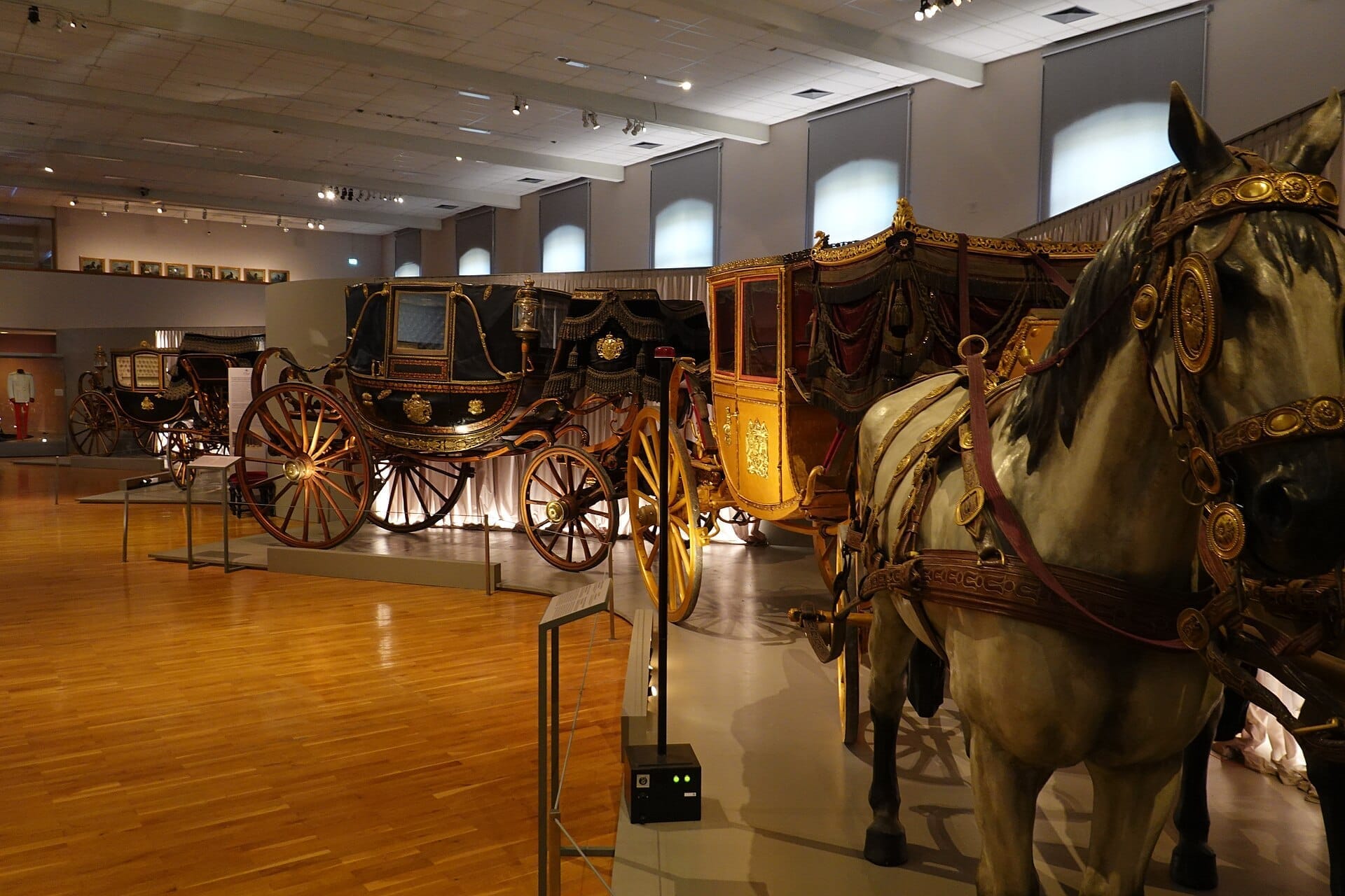 Historische königliche Kutschen und ein eingespanntes Pferd auf Hochglanzholzböden in der Kaiserlichen Wagenburg in Wien.