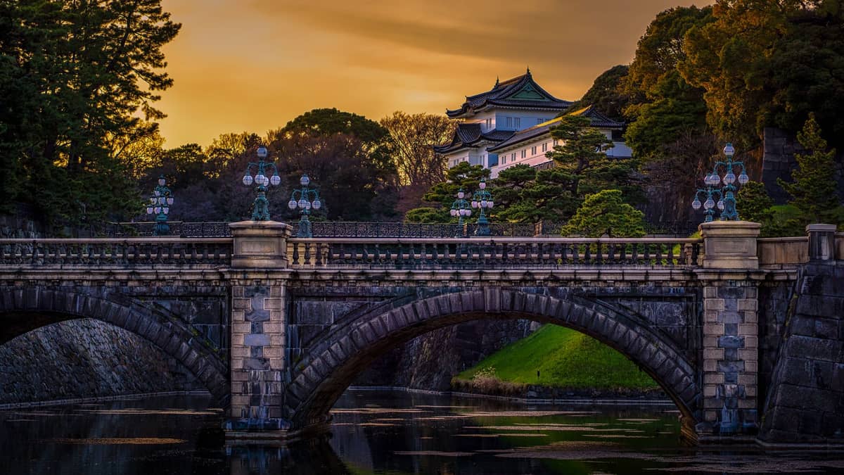 The iconic stone bridge and main gate with the Imperial Palace building and lush greenery in Chiyoda, Tokyo at sunset.