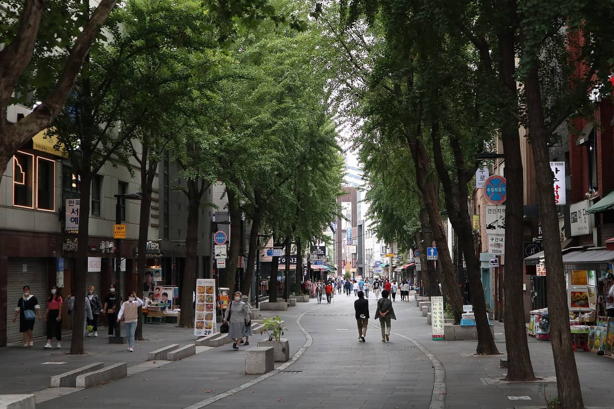 Rua de pedestres em Insa-dong ladeada de árvores e lojas tradicionais, com pessoas caminhando tranquilamente e explorando a área cultural de Seul.