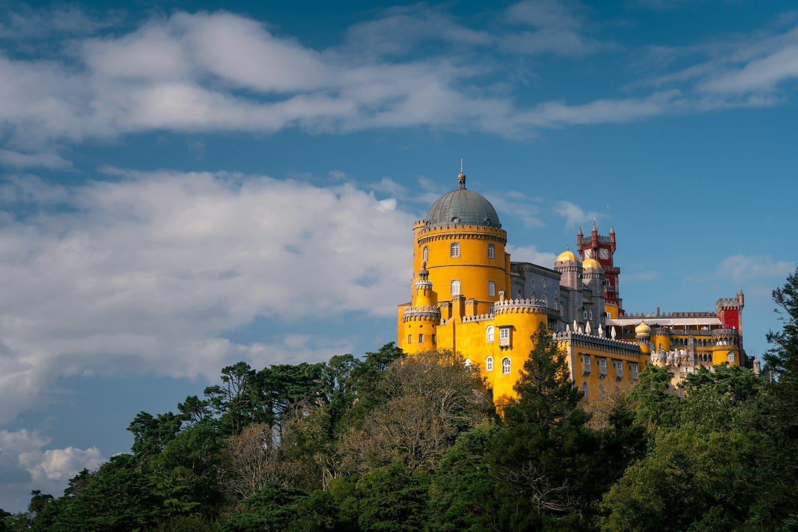 Vue panoramique du coloré Palais de la Pena perché au sommet d'une colline boisée verdoyante sous un ciel bleu avec des nuages épars près de Lisbonne.