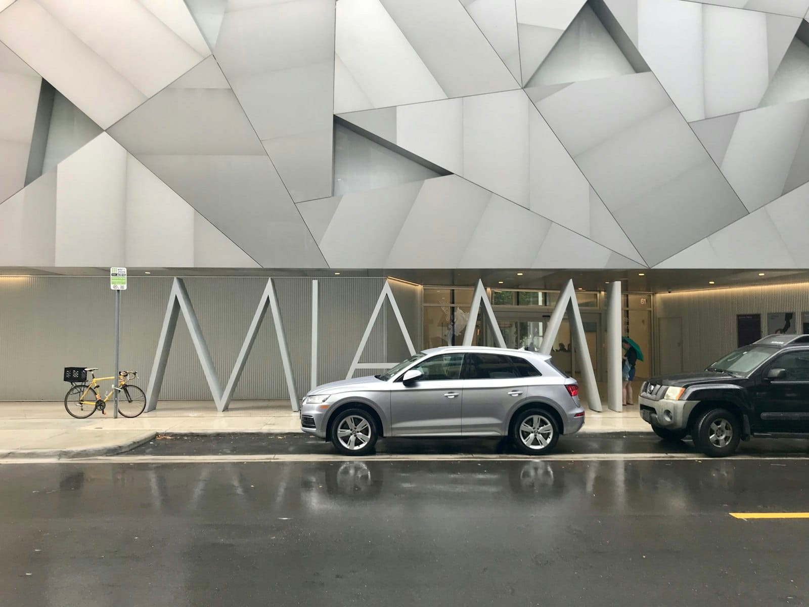 Esterno dell'Institute of Contemporary Art Miami con la facciata geometrica moderna, alcune auto parcheggiate e una bicicletta in una giornata di pioggia.