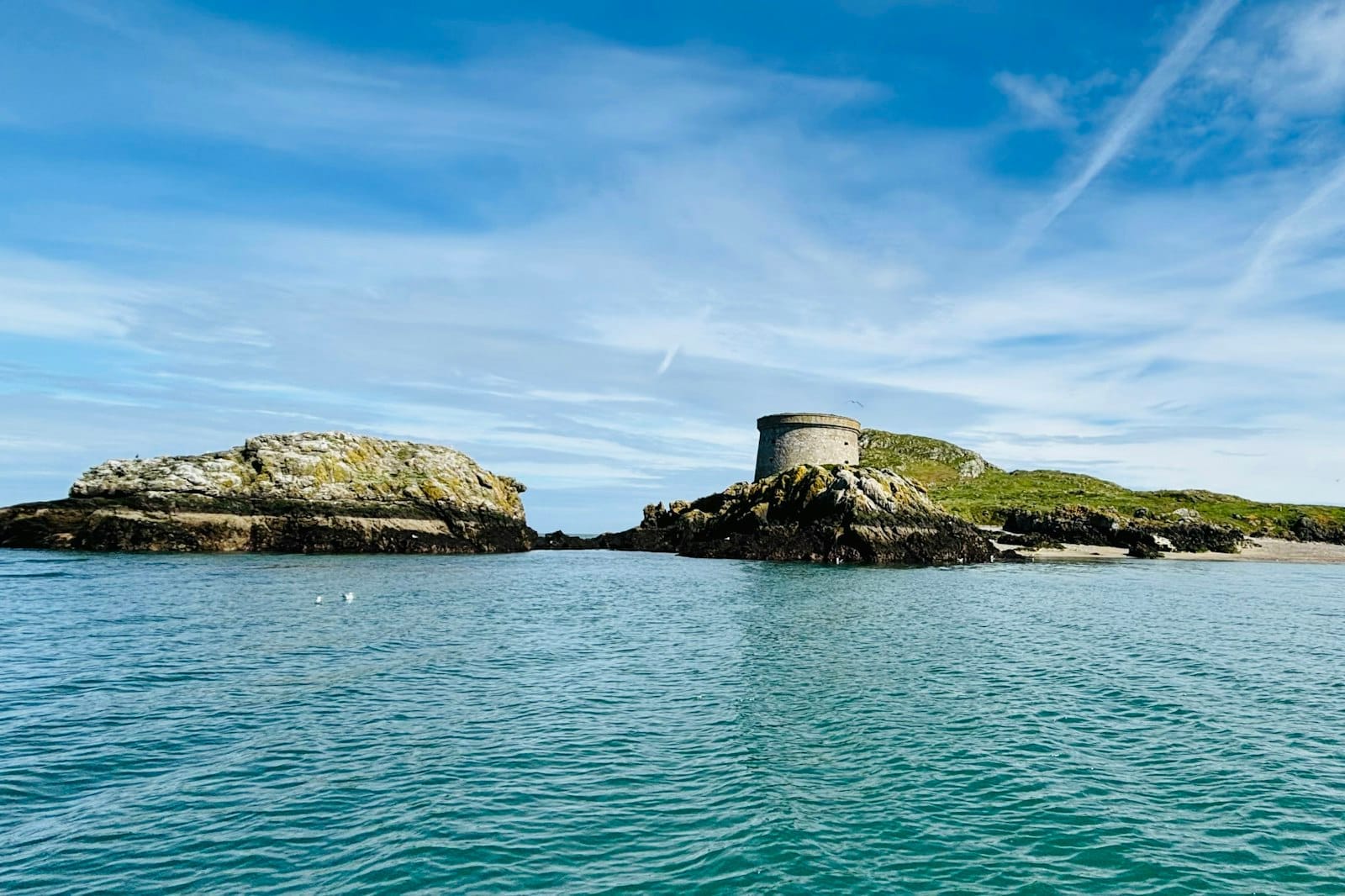 La torre Martello arroccata sugli scogli di Ireland's Eye, circondata da un mare turchese sotto un cielo drammatico, che mostra tutta la bellezza selvaggia e remota dell'isola.