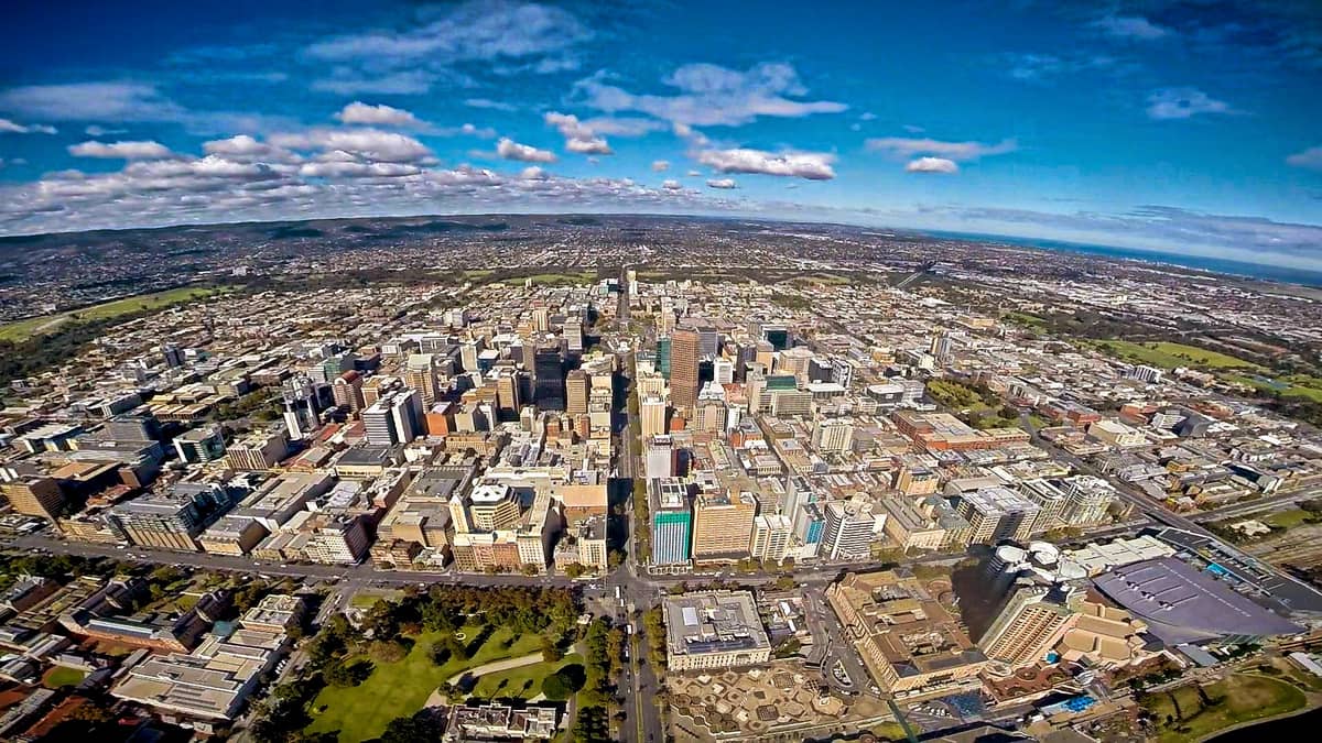 Vista aérea del centro de la ciudad de Adelaide, que muestra su trazado en cuadrícula rodeado de parques, con colinas y costa en la distancia.
