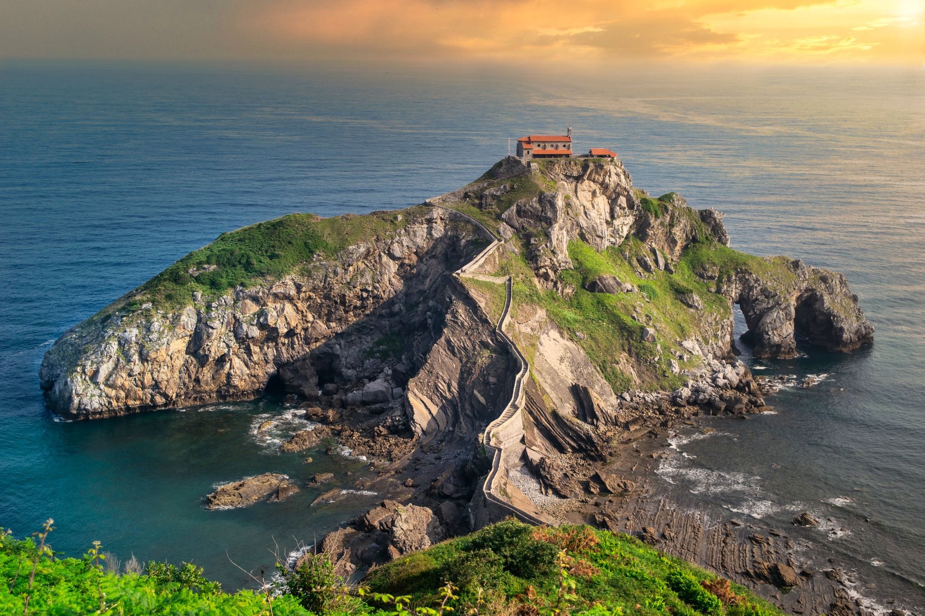 Un'isola rocciosa spettacolare con un tortuoso ponte in pietra e un piccolo eremo che si affaccia sul mare al tramonto, vicino a Bilbao nei Paesi Baschi.