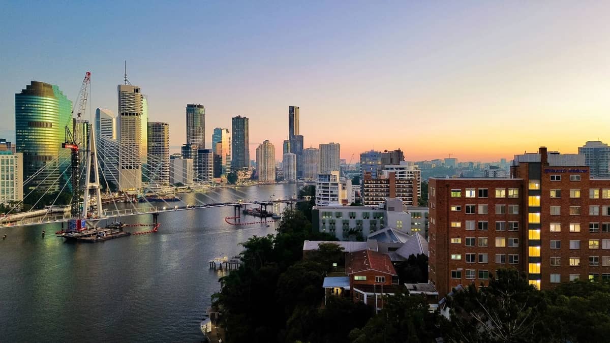 Weitwinkelansicht der Skyline von Brisbane mit Wolkenkratzern, Fluss, Brückenbau und umliegenden Stadtvierteln bei Sonnenuntergang.