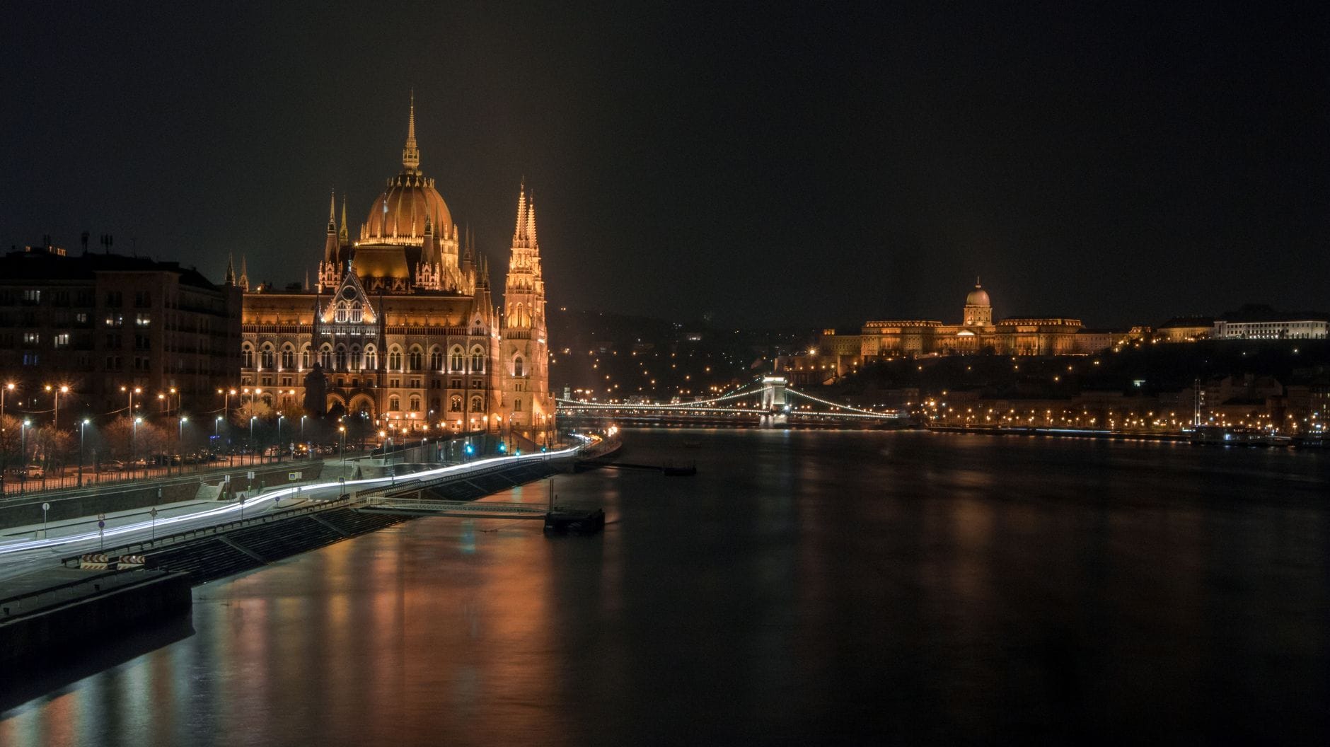 Vista notturna di Budapest con il palazzo del Parlamento illuminato, il Ponte delle Catene e il Castello di Buda riflessi sul fiume Danubio.