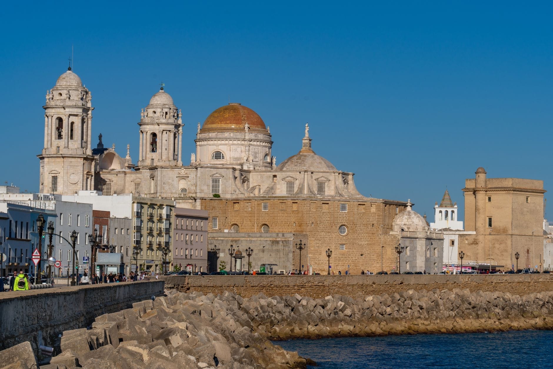 Khung cảnh nổi bật của Nhà thờ Cádiz với mái vòm vàng vươn cao trên đường ven biển và các tòa nhà phố cổ dưới bầu trời xanh trong.