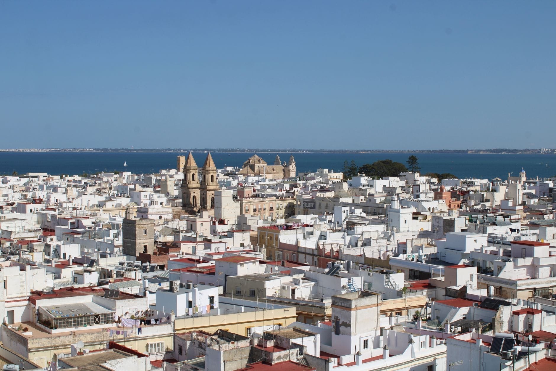 Cảnh rộng của Cádiz với những tòa nhà màu trắng, tháp nhà thờ và Đại Tây Dương ở phía xa dưới bầu trời xanh trong.