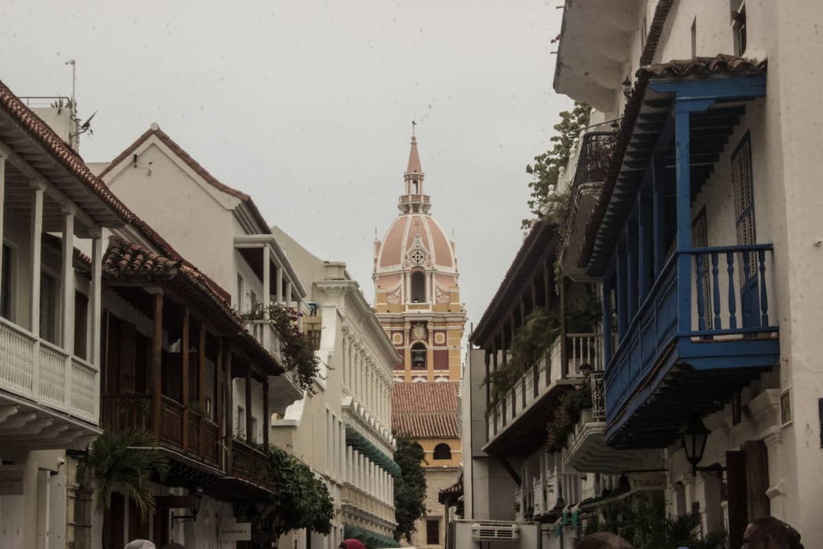 Street scene in Cartagena, Colombia, showing colonial buildings and the iconic cathedral dome in the background.
