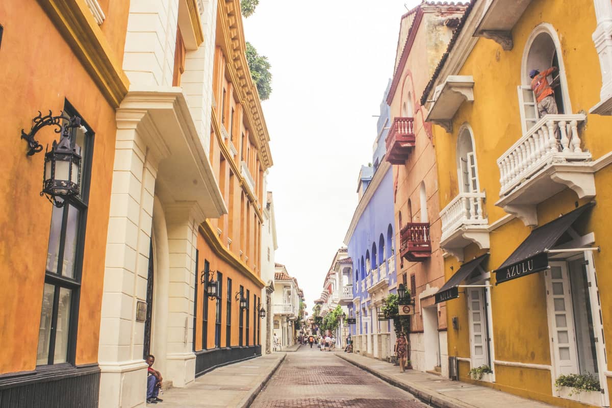 A narrow street in Cartagena, Colombia, lined with colorful colonial buildings, balconies, and small plants, capturing the city's charming atmosphere.