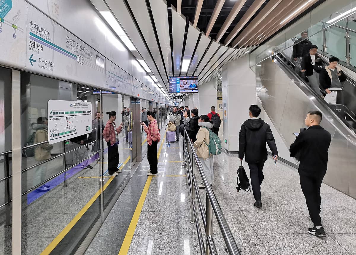 Fahrgäste warten auf einen Zug auf dem Bahnsteig der Chengdu Metro Linie 18, mit klarer Beschilderung und modernem Stationsinneren.