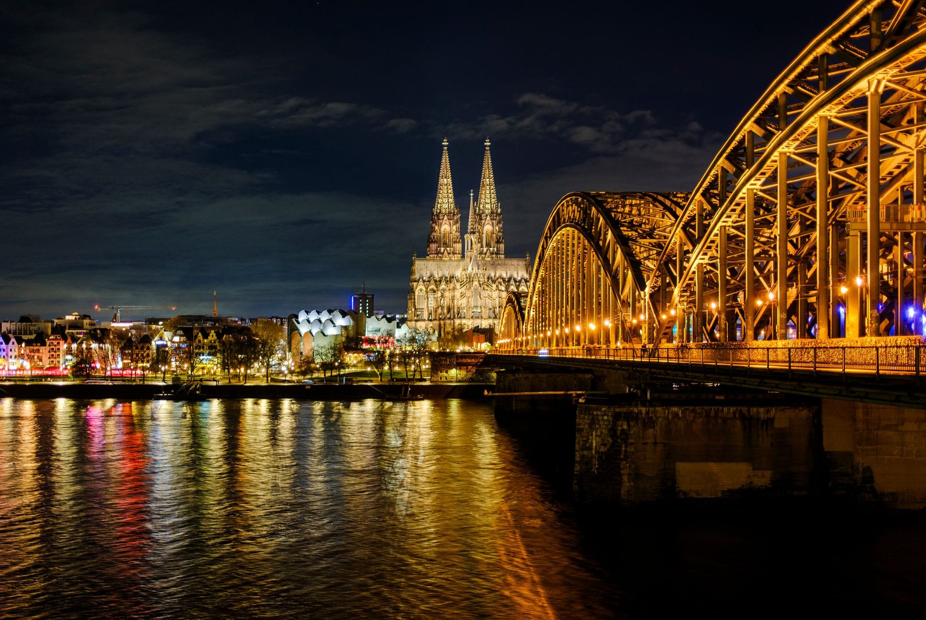 วิวตอนกลางคืนของมหาวิหารโคโลญจน์และสะพาน Hohenzollern ที่มีแสงไฟสะท้อนลงแม่น้ำไรน์ในเมืองโคโลญจน์ ประเทศเยอรมนี