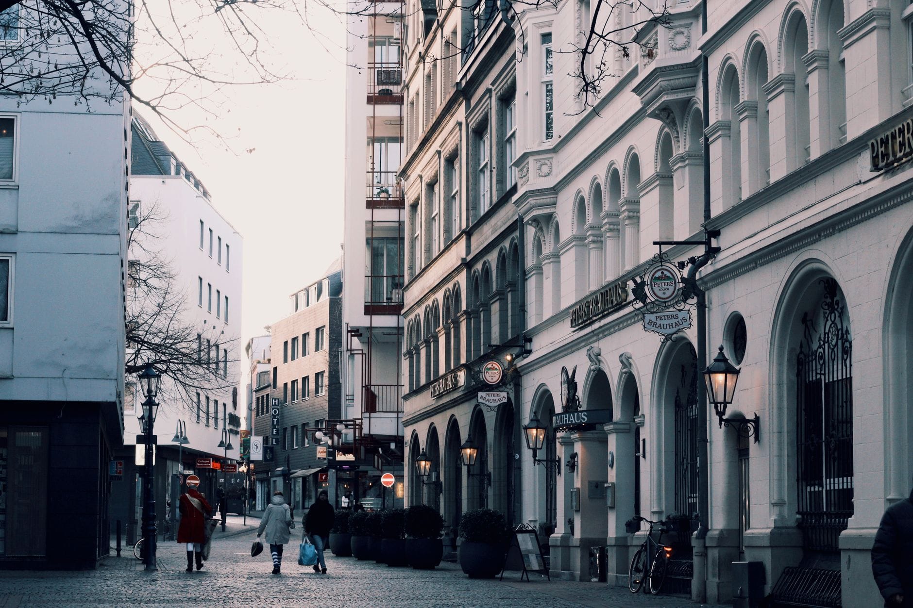 ถนนในย่าน Altstadt ของเมือง Cologne ที่มีผู้คนเดินผ่านอาคารประวัติศาสตร์ ร้านอาหาร และคาเฟ่บนซอยหินกาบที่เงียบสงบ