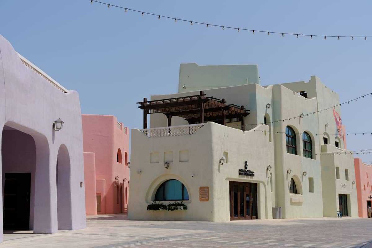 Bunte Pastellgebäude in einer Fußgängerzone mit klarem Himmel, die moderne katarische Architektur in Doha zeigen.