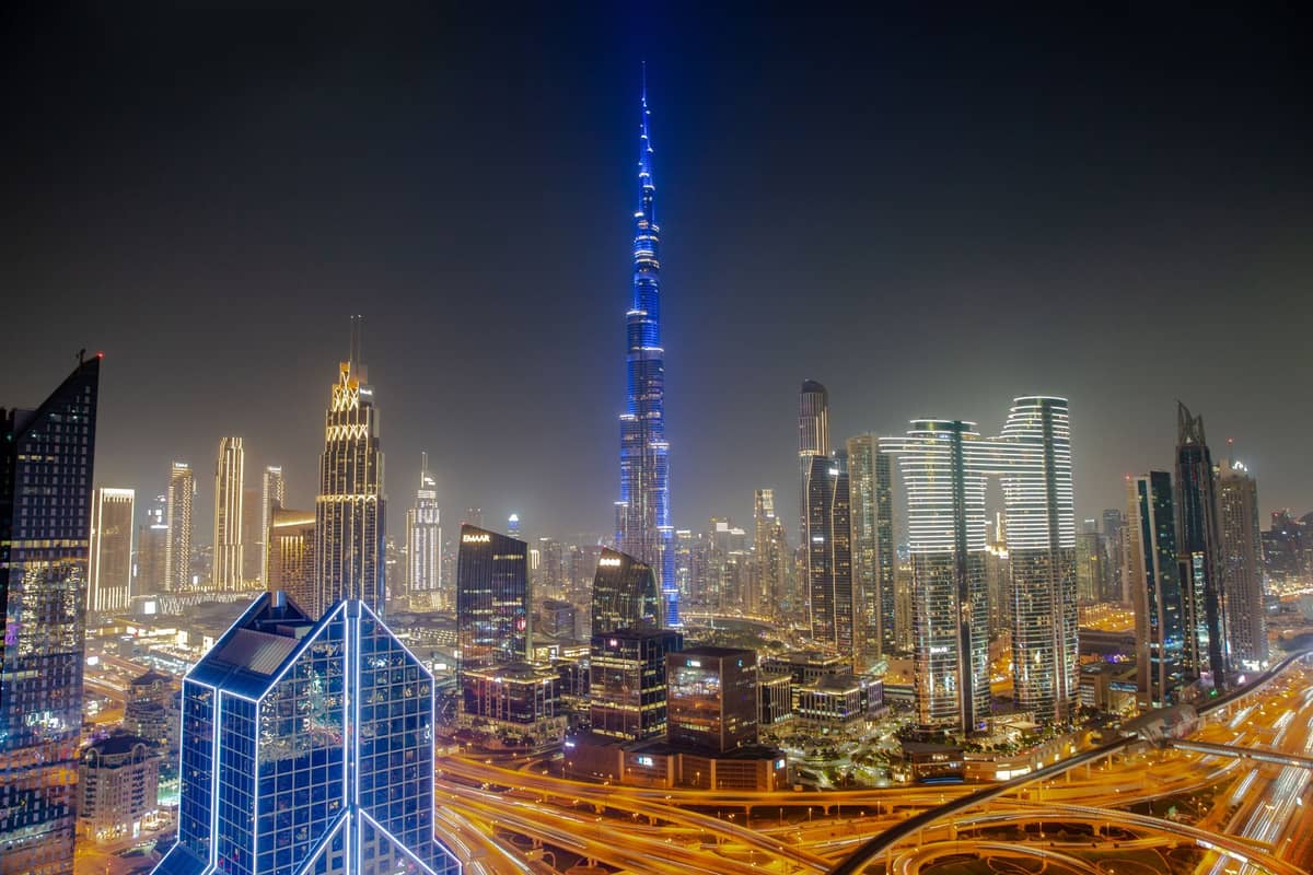 เส้นขอบฟ้าของดูไบยามค่ำคืนพร้อมกับ Burj Khalifa และตึกระฟ้าสมัยใหม่ ทางหลวงที่พลุกพล่านสว่างไสวด้วยไฟถนนสีเหลืองและแสงไฟรถที่แล่นผ่าน