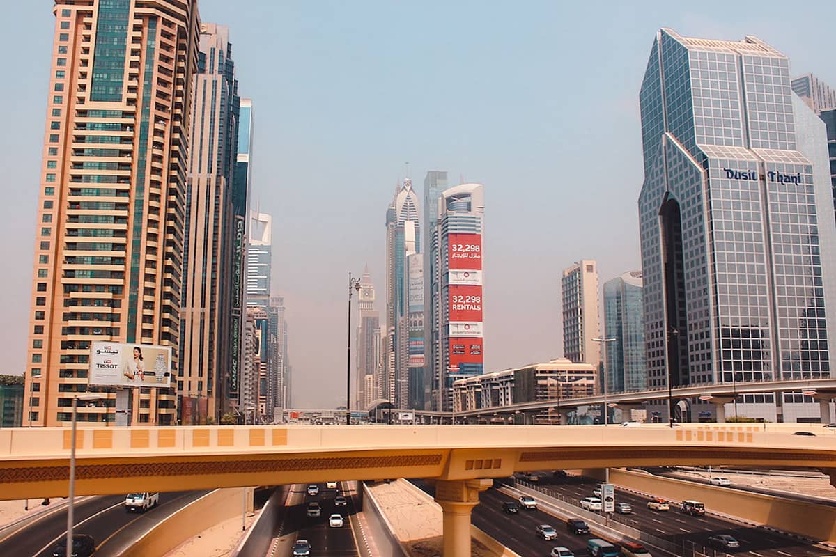 Wolkenkratzer und Luxushotels im Downtown Dubai entlang der Sheikh Zayed Road, an einem dunstigen Tag über eine belebte Autobahn und eine Überführung hinweg fotografiert.