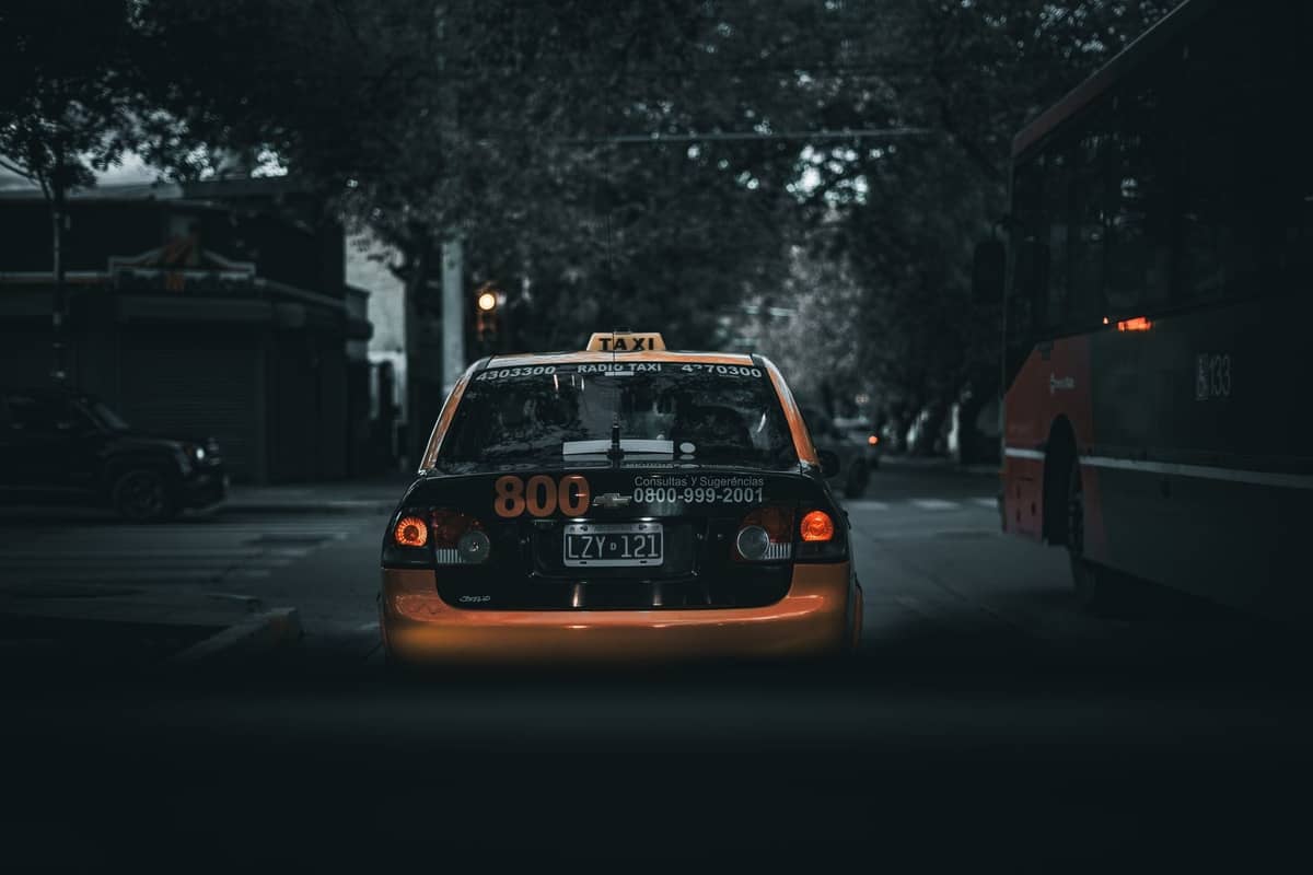 Ein Taxi aus Guadalajara auf einer Stadtstraße in der Abenddämmerung, von hinten gesehen, mit einem Bus und Autos in der Nähe.