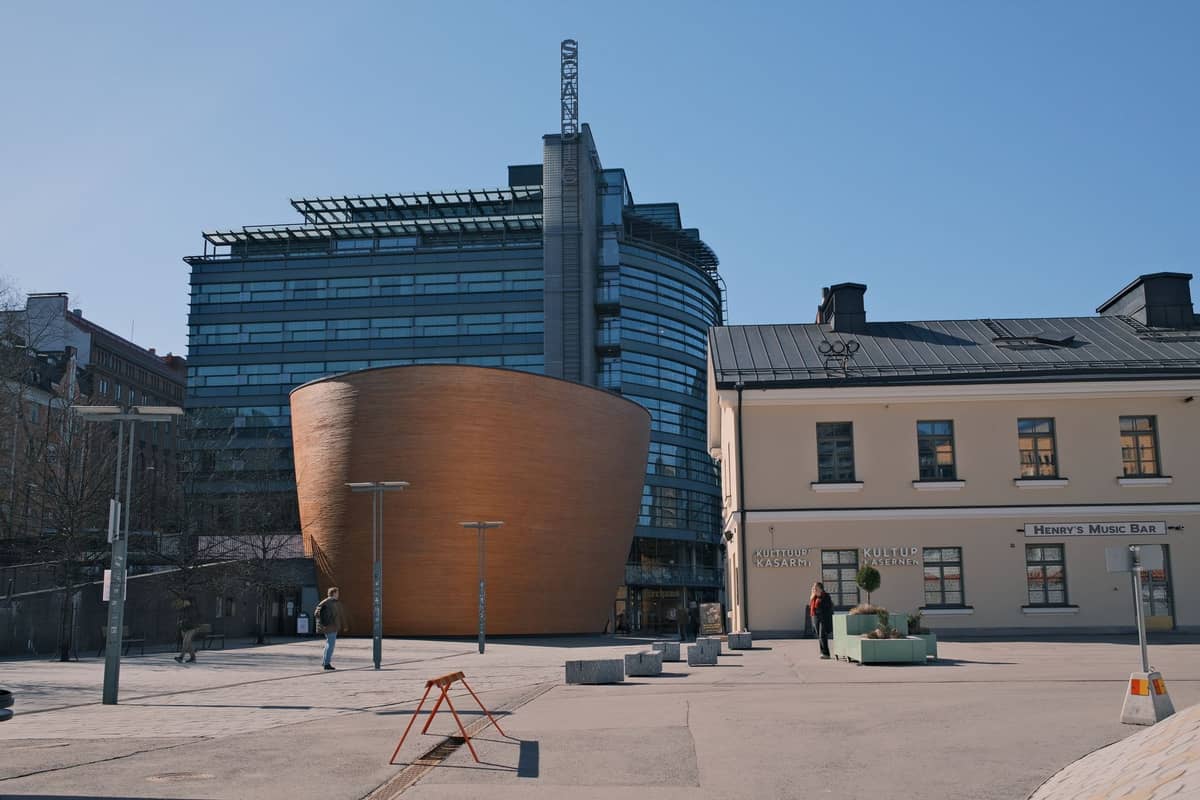 Paisagem urbana moderna de Helsinque com a marcante Kamppi Chapel of Silence de madeira, edifício de escritórios de vidro e praça sob um céu azul limpo