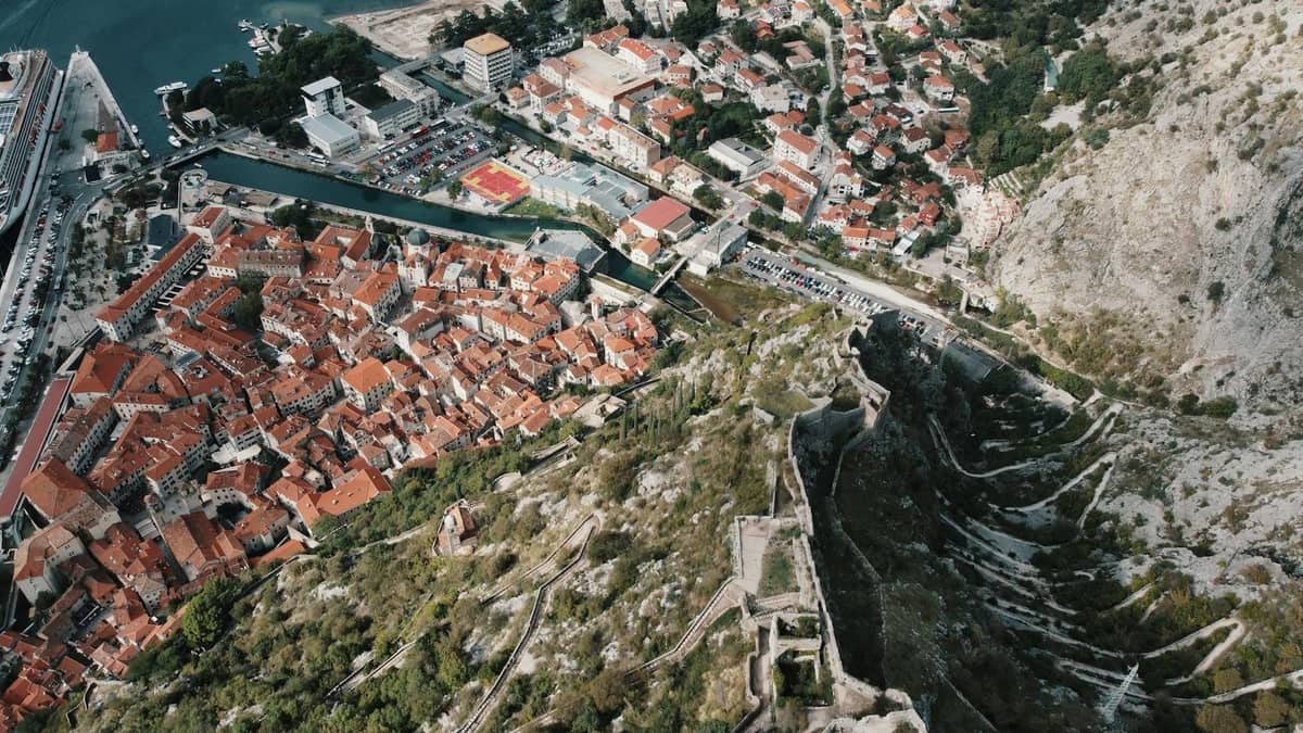 Aerial view of Kotor showing the red-roofed old town, fortress walls climbing the mountain, and harbor area, well illustrating the city’s layout.