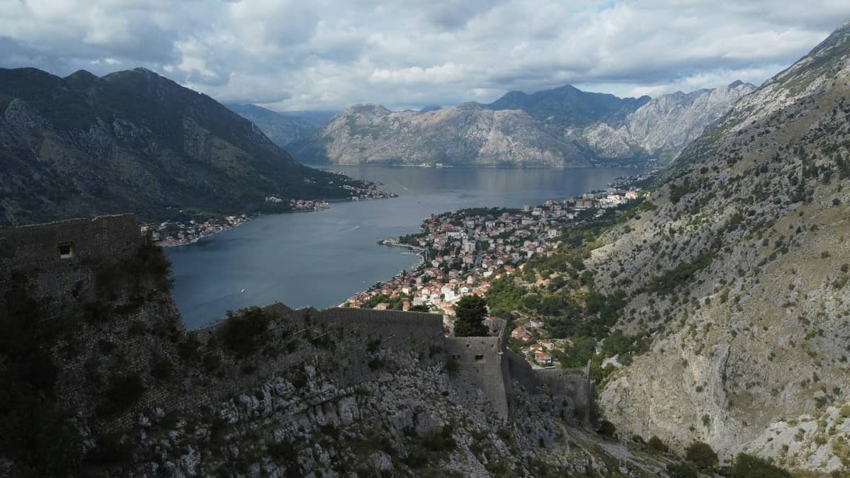 A dramatic view over the Bay of Kotor with steep mountains, the walled old town, and calm blue water at the innermost point of the fjord-like bay.