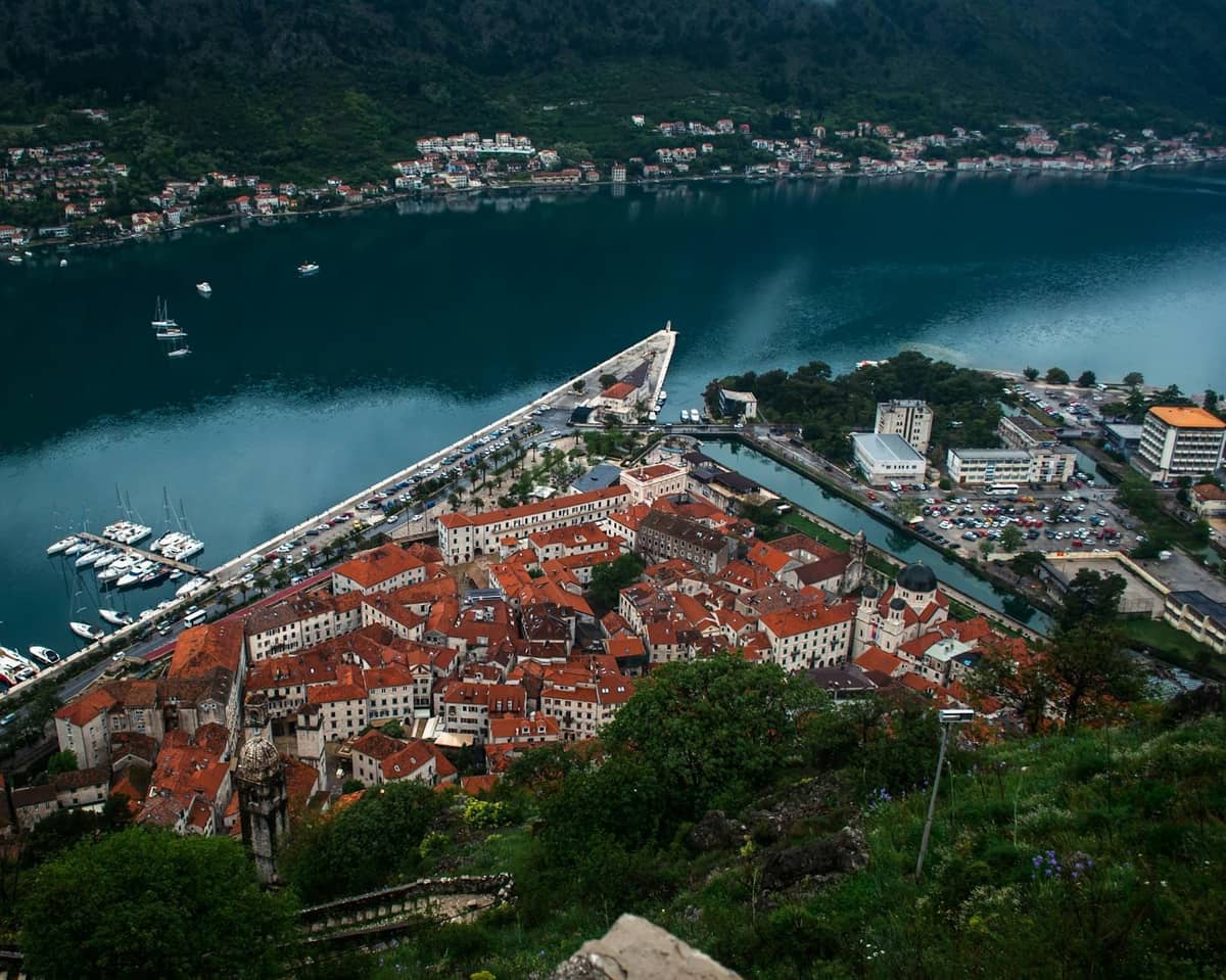 Elevated view of Kotor old town with red rooftops and the bay, surrounded by mountains, showing the city walls and waterfront.