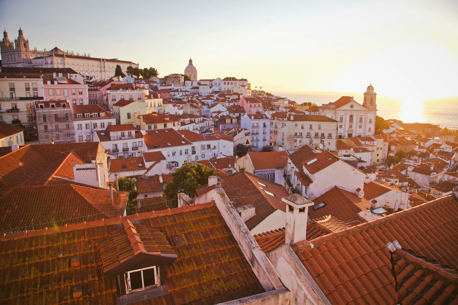 Vue panoramique sur les toits de l'Alfama à Lisbonne et le fleuve au lever du soleil, monuments et dôme visibles dans la lumière dorée de l'heure dorée.