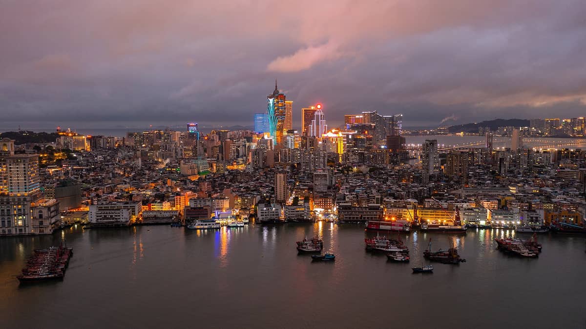 Weite Luftaufnahme der Skyline von Macau in der Abenddämmerung mit der Uferpromenade, Casinos, der belebten Stadtlandschaft und dem markanten beleuchteten Grand Lisboa-Gebäude.