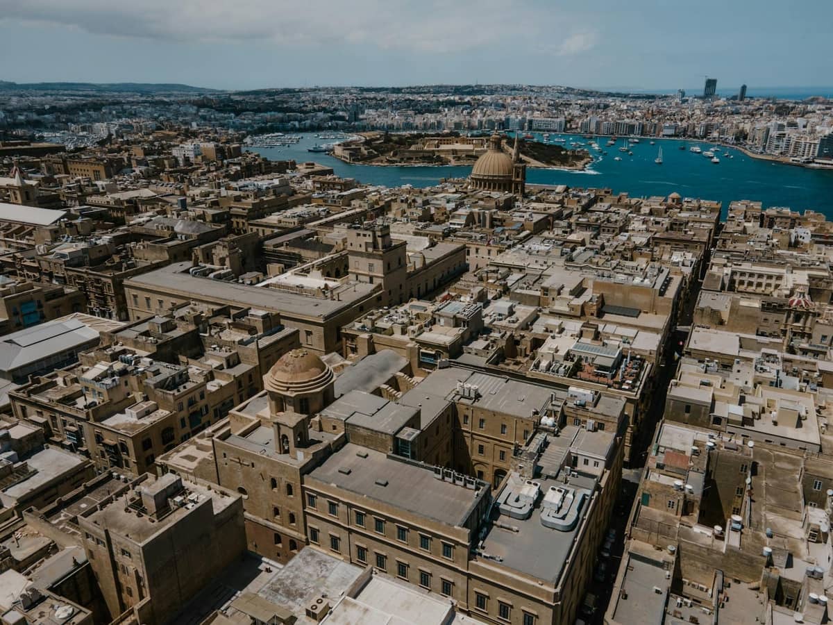 Vista aerea di Malta con storici edifici in pietra, chiese a cupola e le acque azzurre del Mediterraneo sullo sfondo.