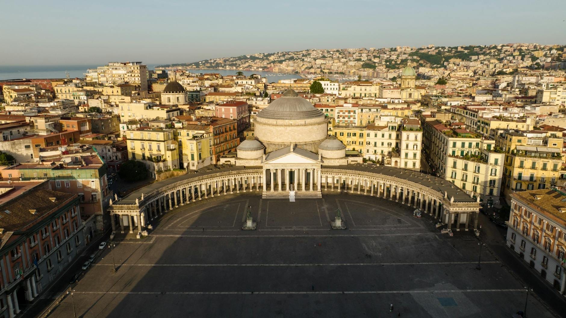 Vue aérienne de la Piazza del Plebiscito à Naples avec la Basilique de San Francesco di Paola et les bâtiments colorés de la ville en arrière-plan.