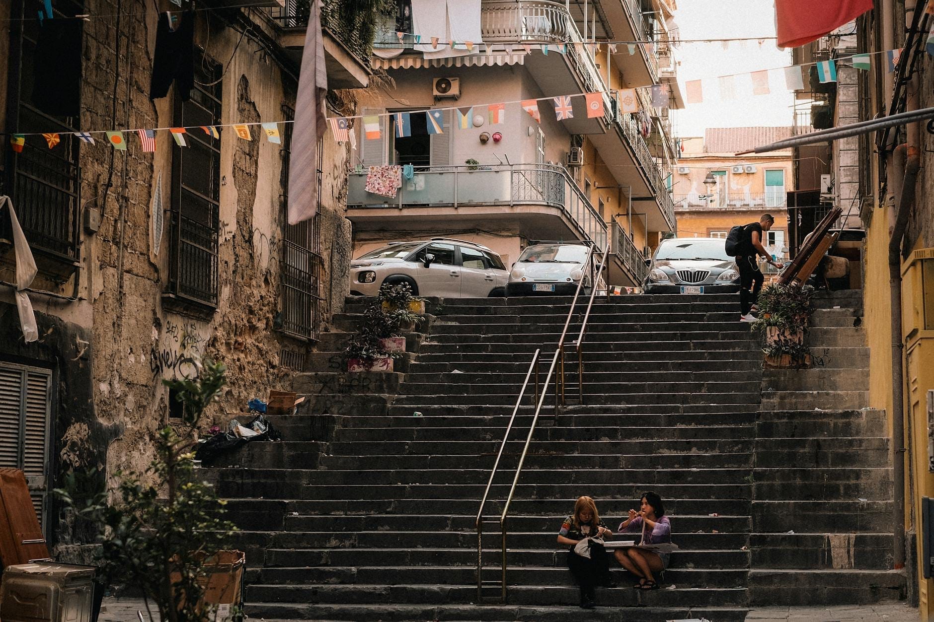 Scène urbaine à Naples avec des escaliers en pierre, des habitants assis et marchant, du linge étendu et une authentique architecture méditerranéenne.