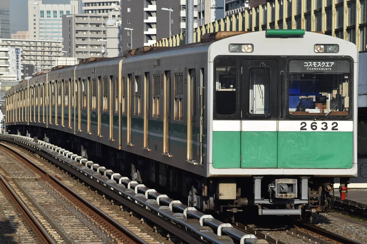 Osaka Metro train on outdoor tracks, with green and white exterior and city buildings in the background.