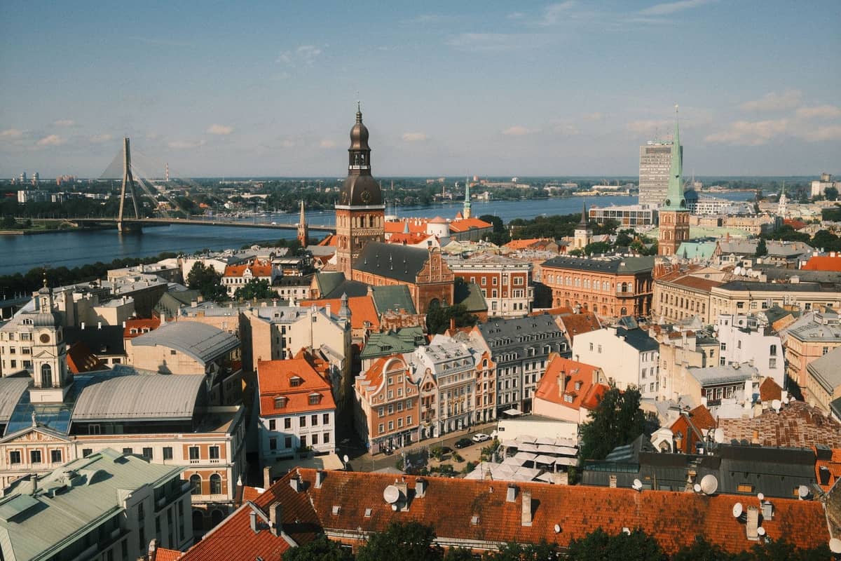Weite Luftaufnahme der Rigaer Altstadt mit roten Dächern, dem Fluss Daugava, dem Dom zu Riga und der modernen Schrägseilbrücke im Hintergrund.