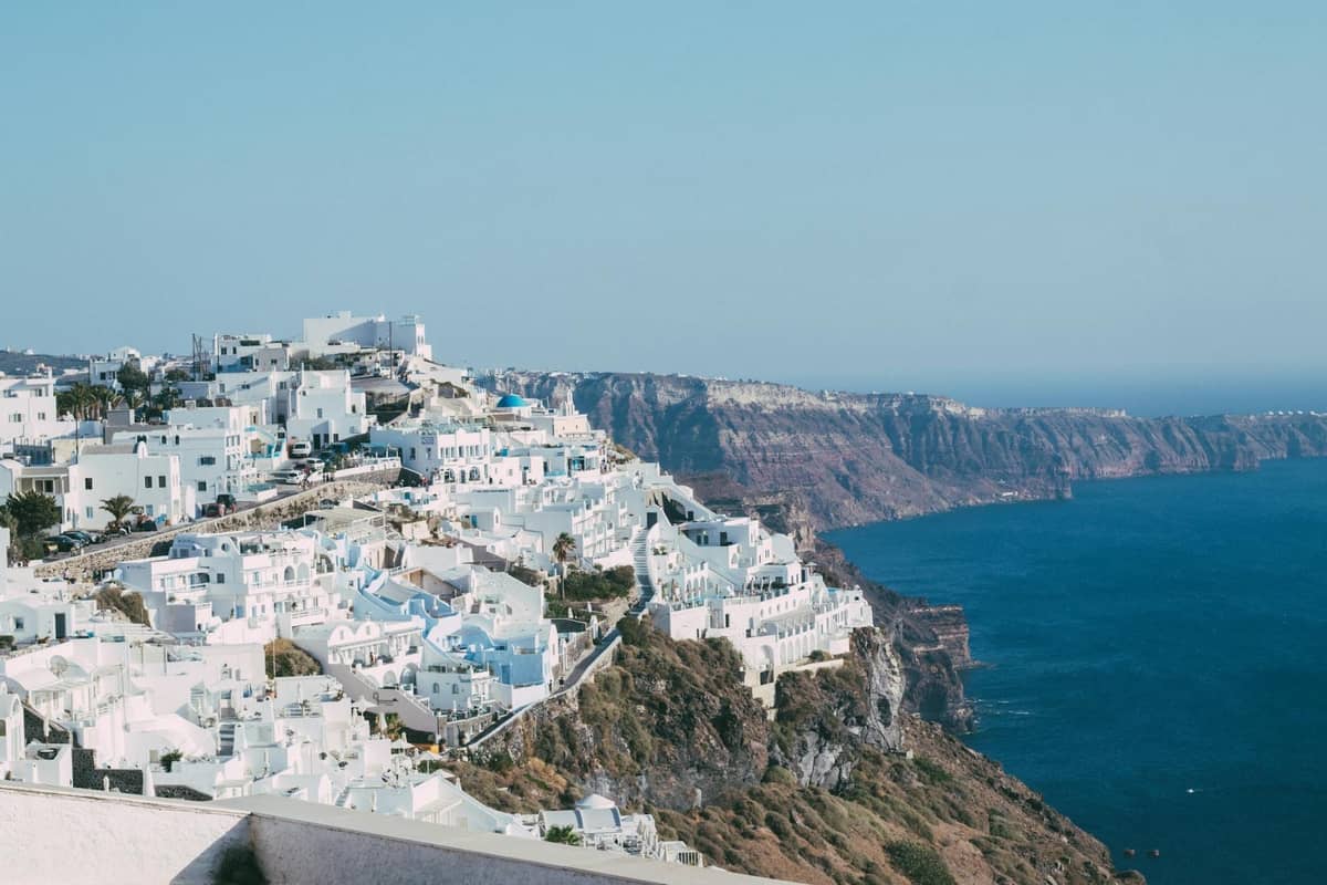Edifici bianchi di Santorini arroccati su scogliere che si affacciano sul profondo mare Egeo azzurro e sul drammatico cratere vulcanico.