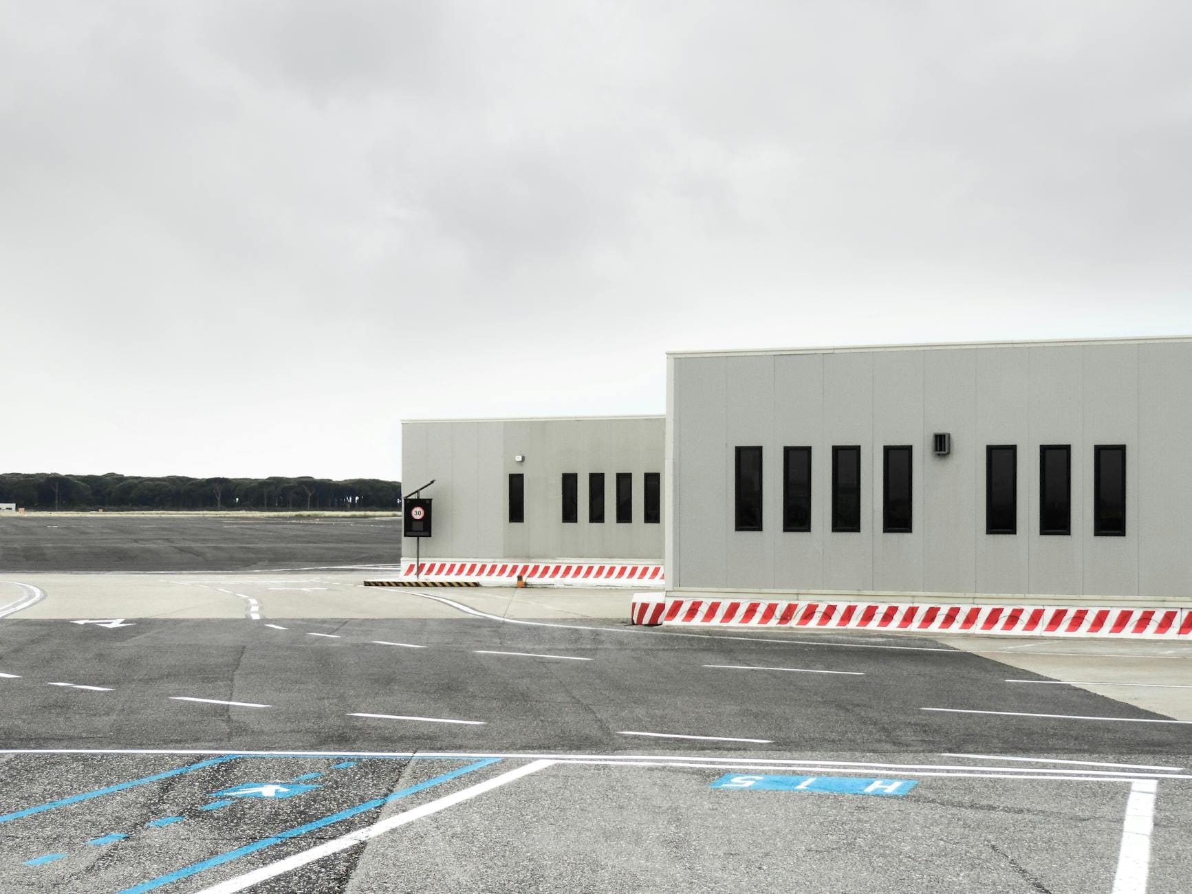 Blick auf ein kleines Flughafenterminalgebäude neben einem leeren Rollfeld unter einem bewölkten Himmel, das Bodentransporteinrichtungen zeigt.