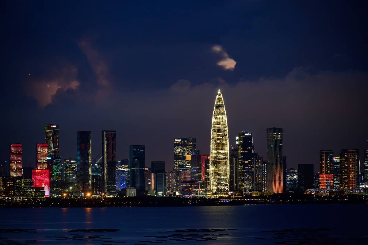 O horizonte moderno de Shenzhen à noite, com a iluminada sede da China Resources e os arranha-céus ao redor refletidos na água, mostrando a vibrante paisagem urbana da cidade.