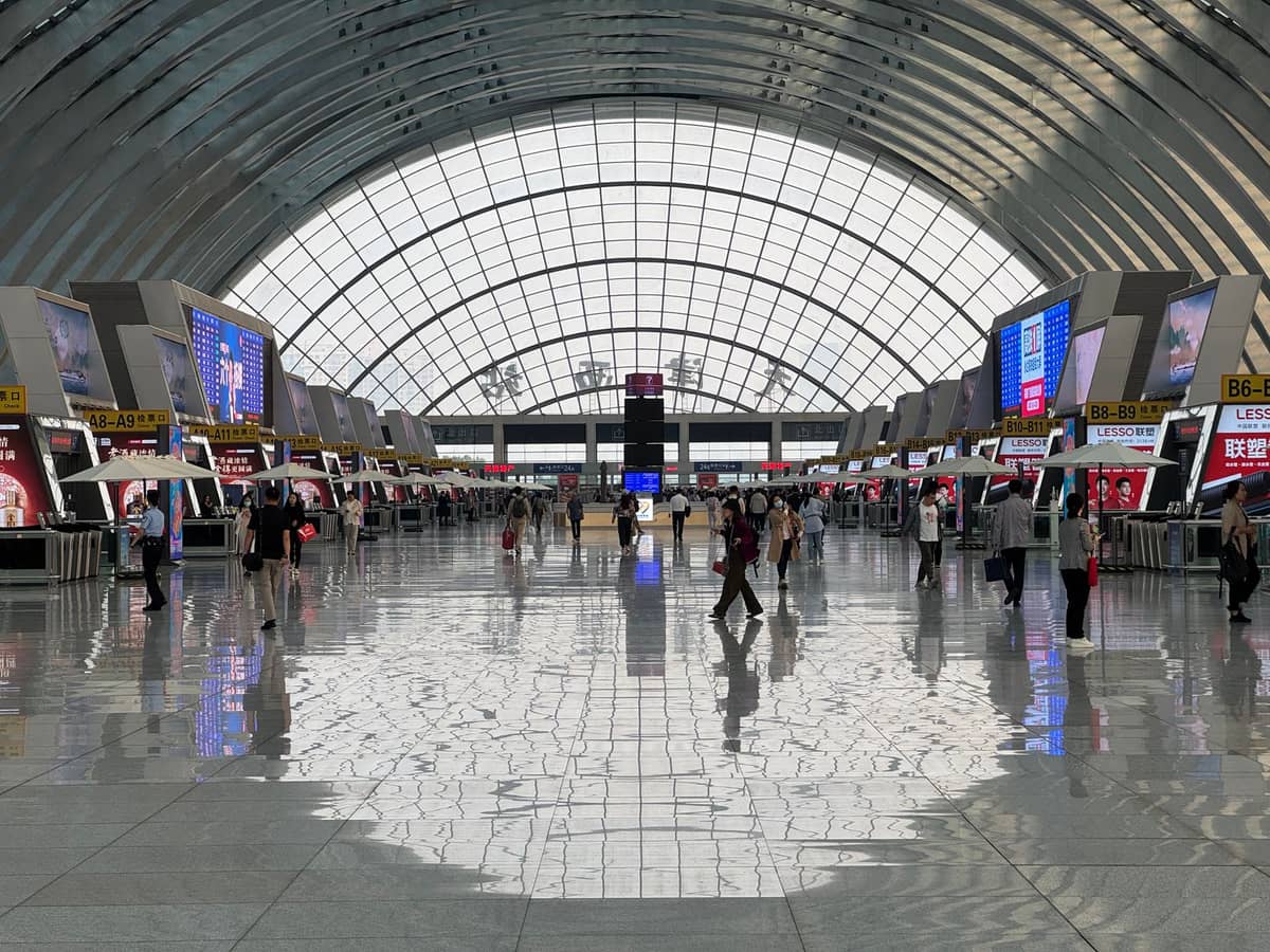 Interior espaçoso e moderno do Aeroporto Internacional de Shenzhen Bao'an com viajantes caminhando entre os balcões de check-in e um grande teto de vidro arqueado acima.
