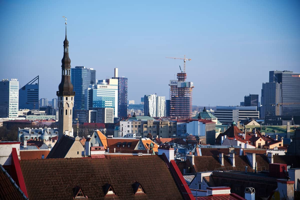 Panorama de Tallinn con los tejados medievales del Casco Antiguo, torres de iglesias y rascacielos modernos al fondo bajo un cielo azul despejado