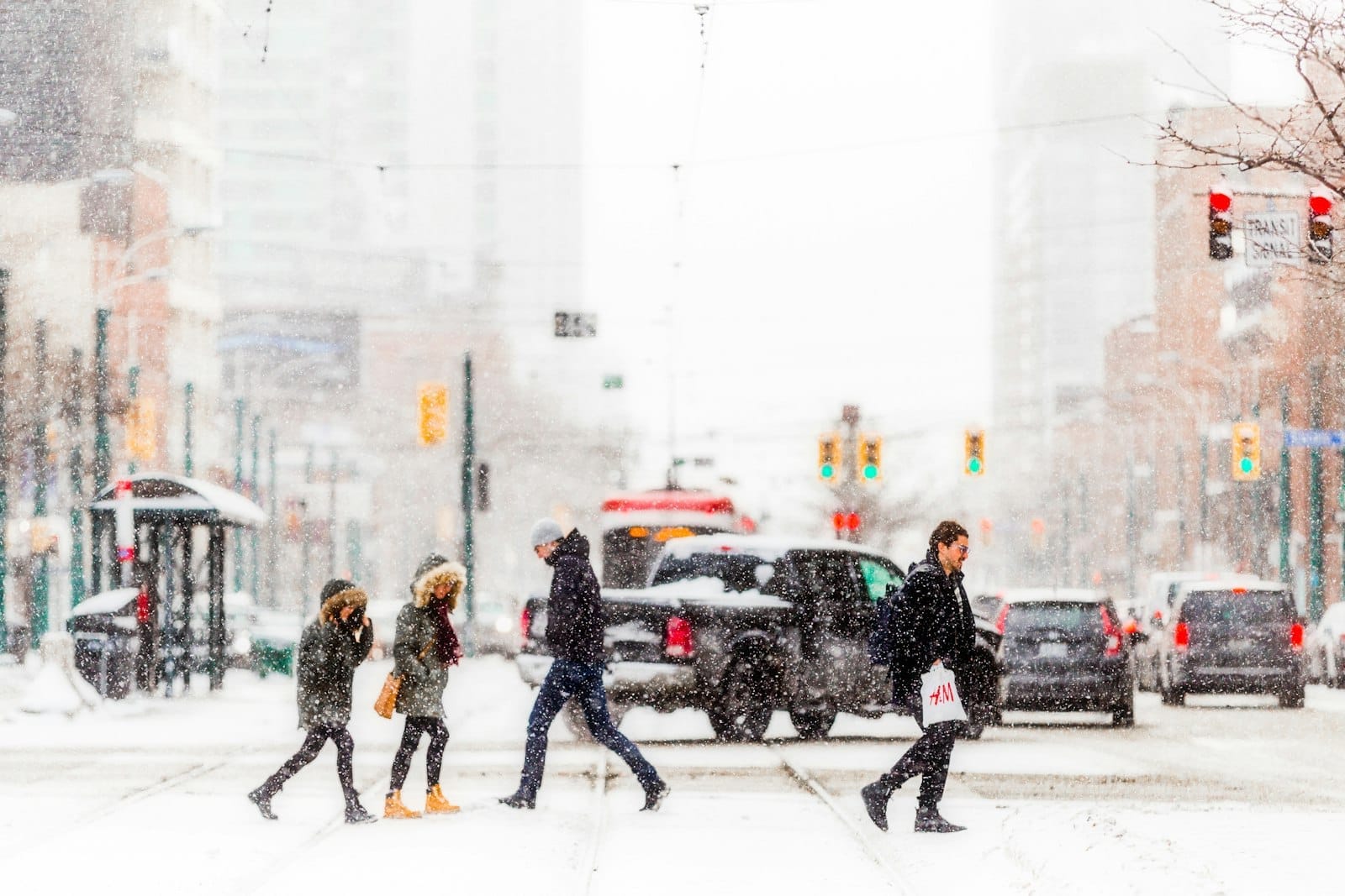 Pedestres agasalhados atravessando uma movimentada rua de Toronto durante uma forte nevasca, com ruas cobertas de neve e semáforos urbanos visíveis.