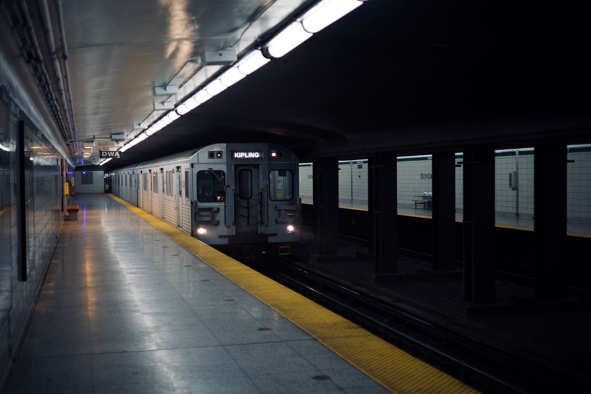 Um trem do metrô TTC chegando a uma estação subterrânea de Toronto com iluminação intensa e linha de segurança amarela.