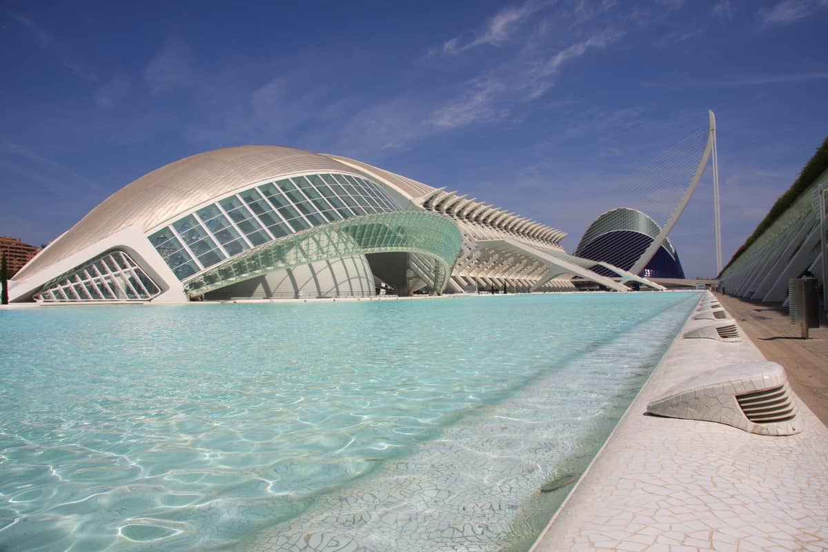 L'edificio futuristico dell'Hemisfèric e le piscine cristalline nella Città delle Arti e delle Scienze di Valencia, sotto un cielo azzurro e soleggiato.