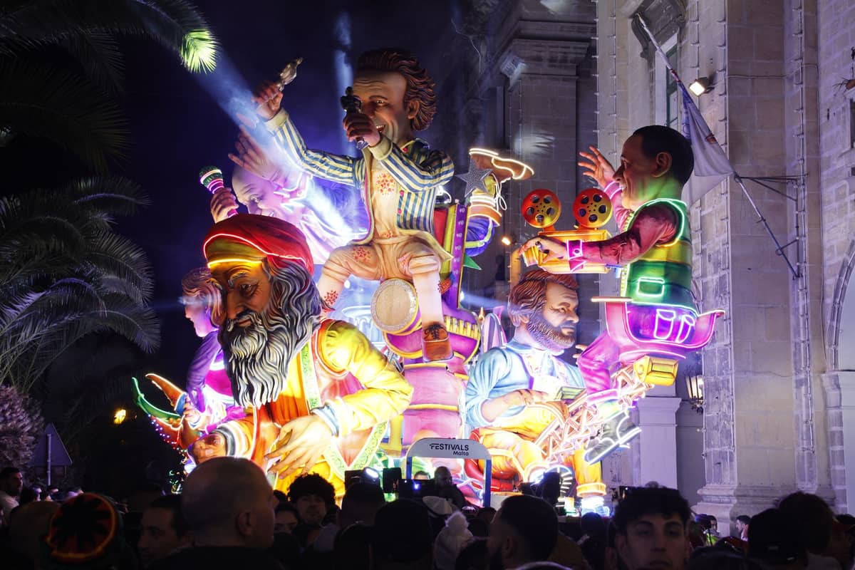 Scena notturna del festival Fallas con grandi sculture ninot illuminate e folle davanti a un edificio storico a Valencia.