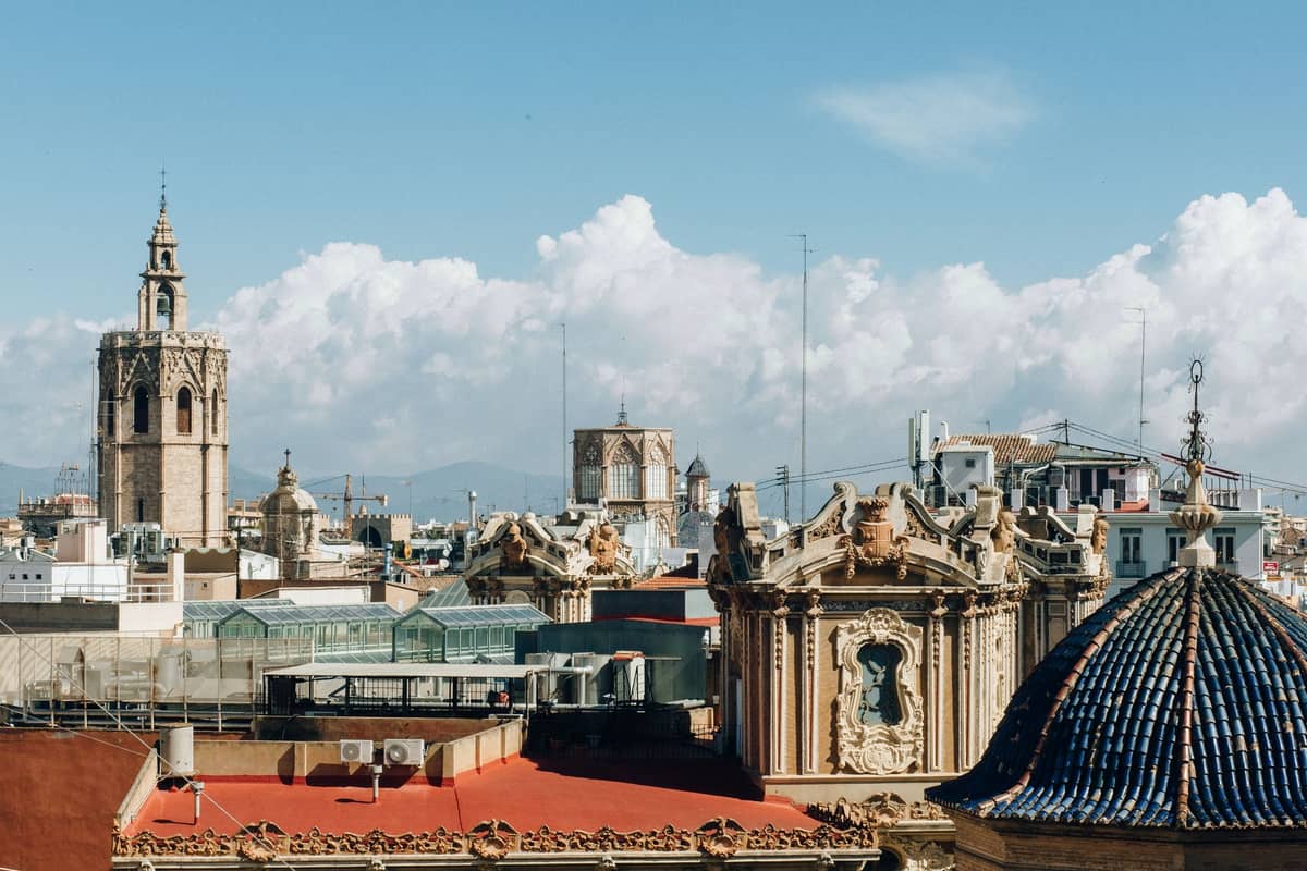 Panorama di Valencia con torri storiche, tetti ornati e architettura mediterranea sotto un cielo azzurro con nuvole.