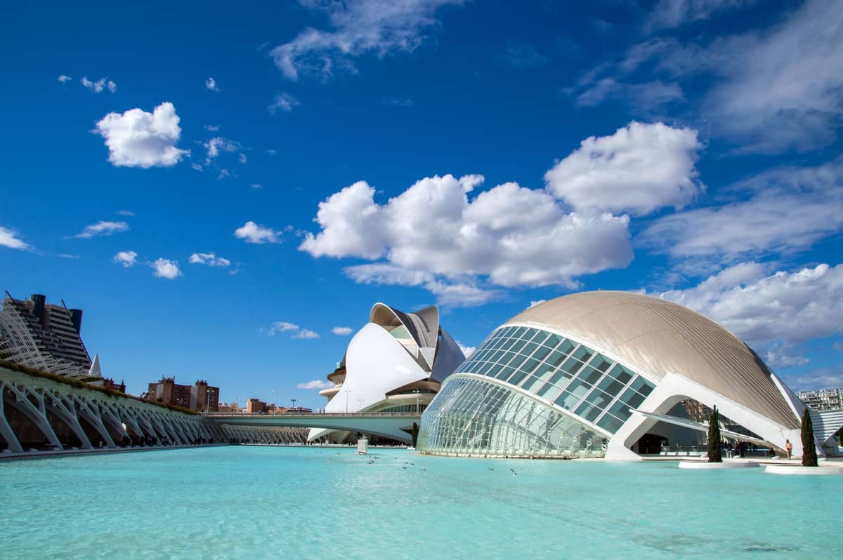 Vista grandangolare del complesso Ciudad de las Artes y las Ciencias di Valencia con moderni edifici bianchi e piscine blu riflettenti sotto un cielo parzialmente nuvoloso.