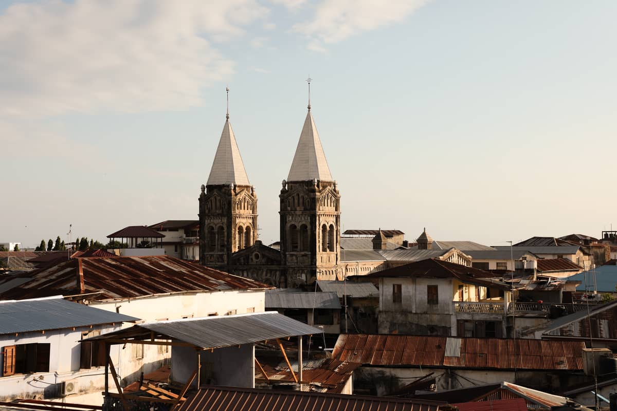 Blick über die Dächer von Stone Town, Sansibar, mit den zwei Türmen der historischen Kathedrale, die im sanften Abendlicht über die umliegenden Gebäude ragen.