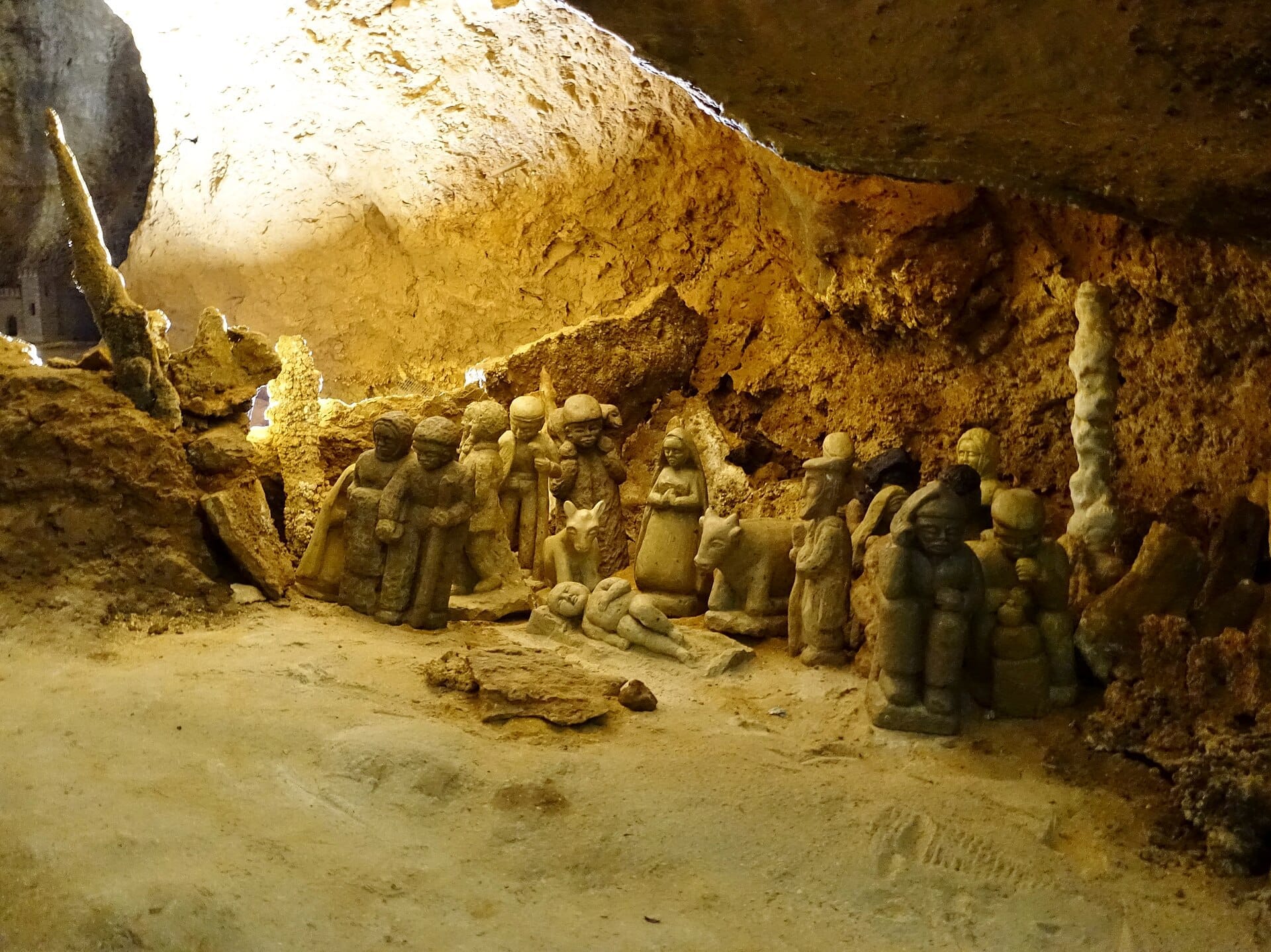 Steinerne Weihnachtskrippe in der ockerfarbenen Dolomit-Höhle von Is Zuddas im Südwesten Sardiniens, beleuchtet von warmem Höhlenlicht.