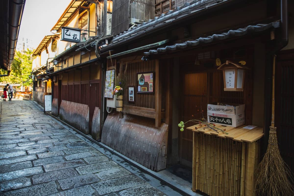 Atmospheric stone-paved alley lined with traditional wooden machiya townhouses and discreet signs, capturing the quiet charm of Ishibe-koji Lane in Kyoto.
